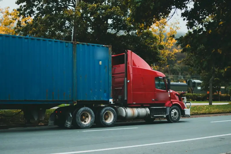 Red semi truck hauling a blue shipping container